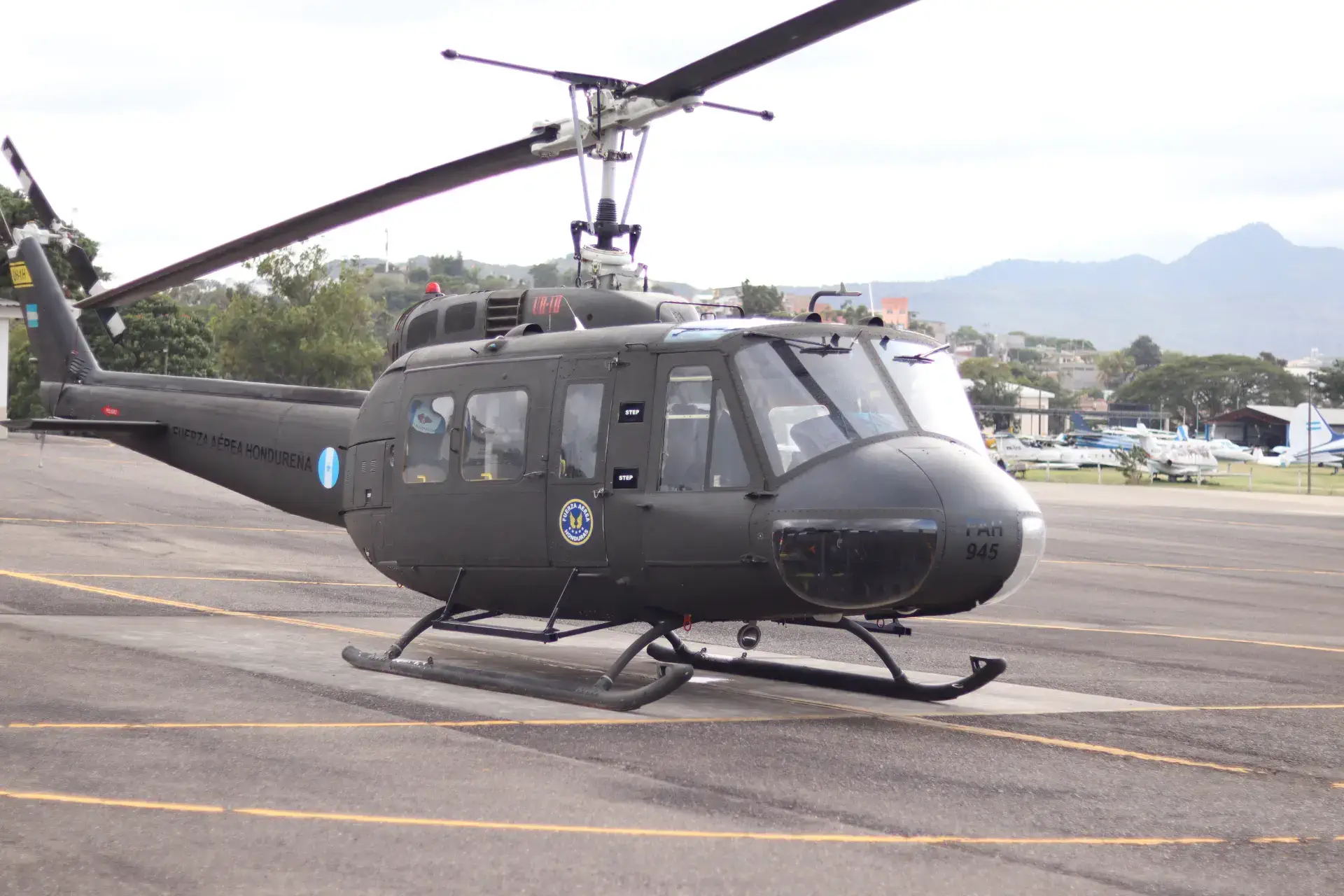 A parked military helicopter on a tarmac with mountains in the background.