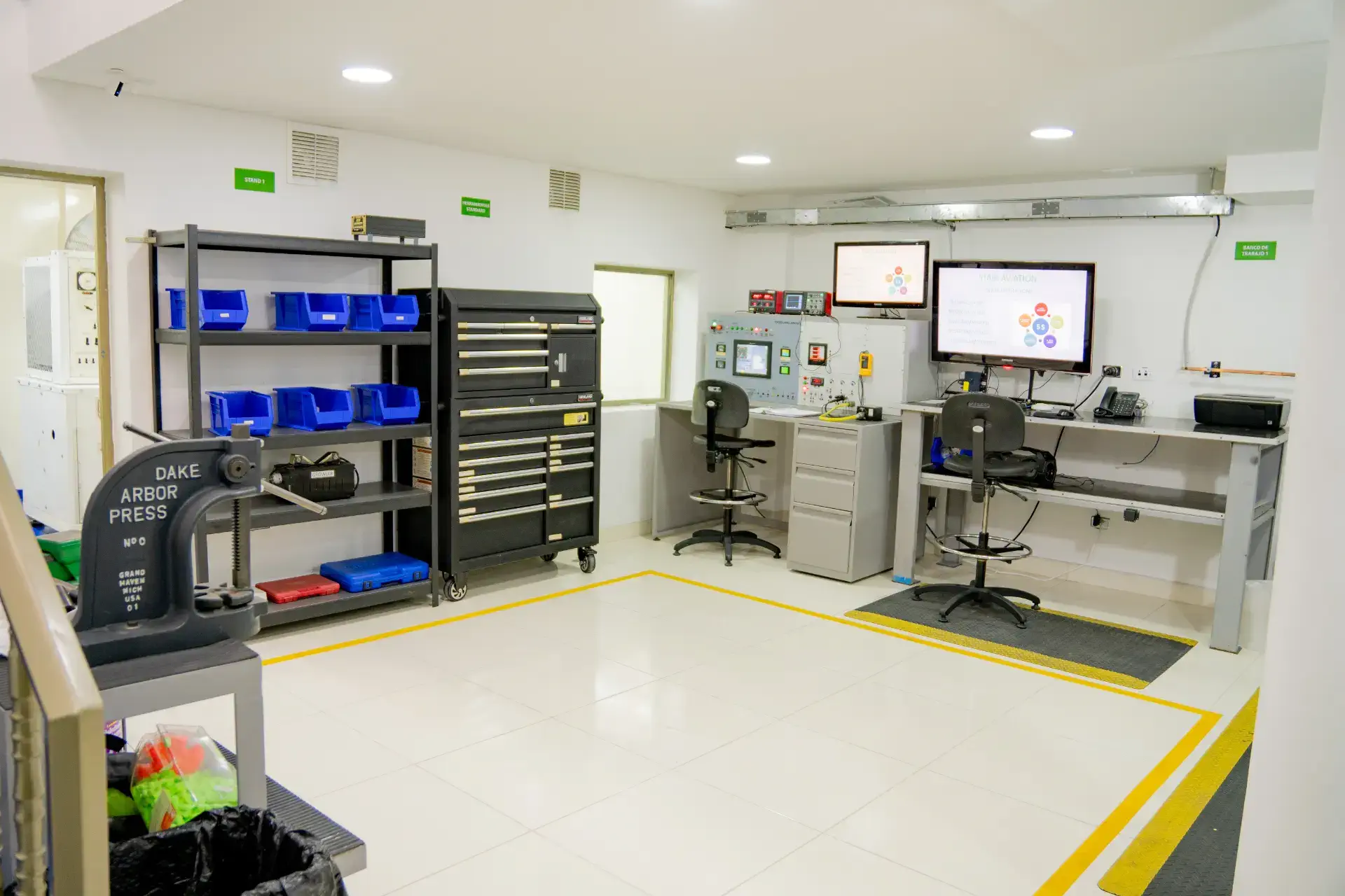 Modern, organized workshop with workbenches, tools, shelves with bins, and instructional screens.