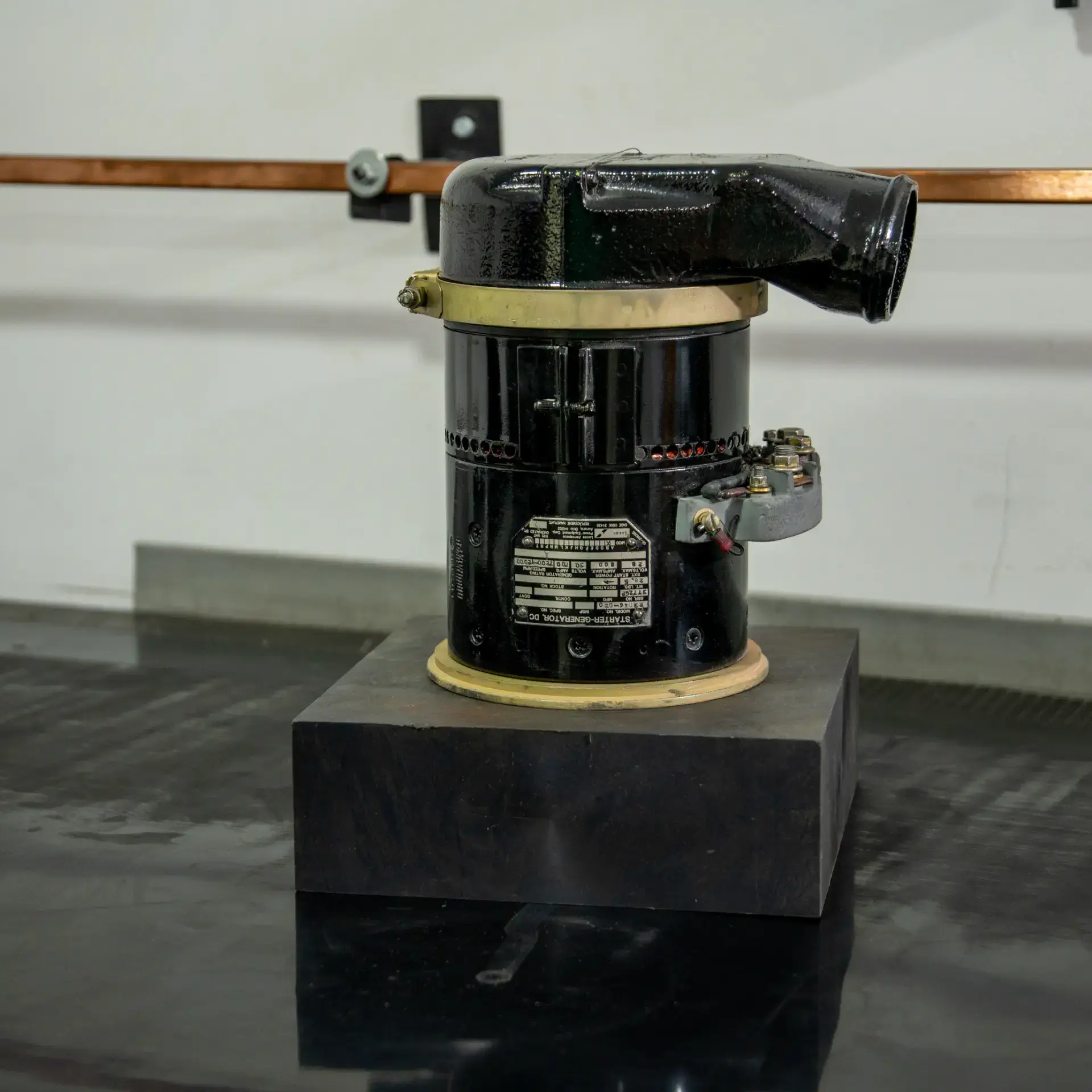 An old-fashioned, black cylindrical electrical device with a label, on a wooden base.