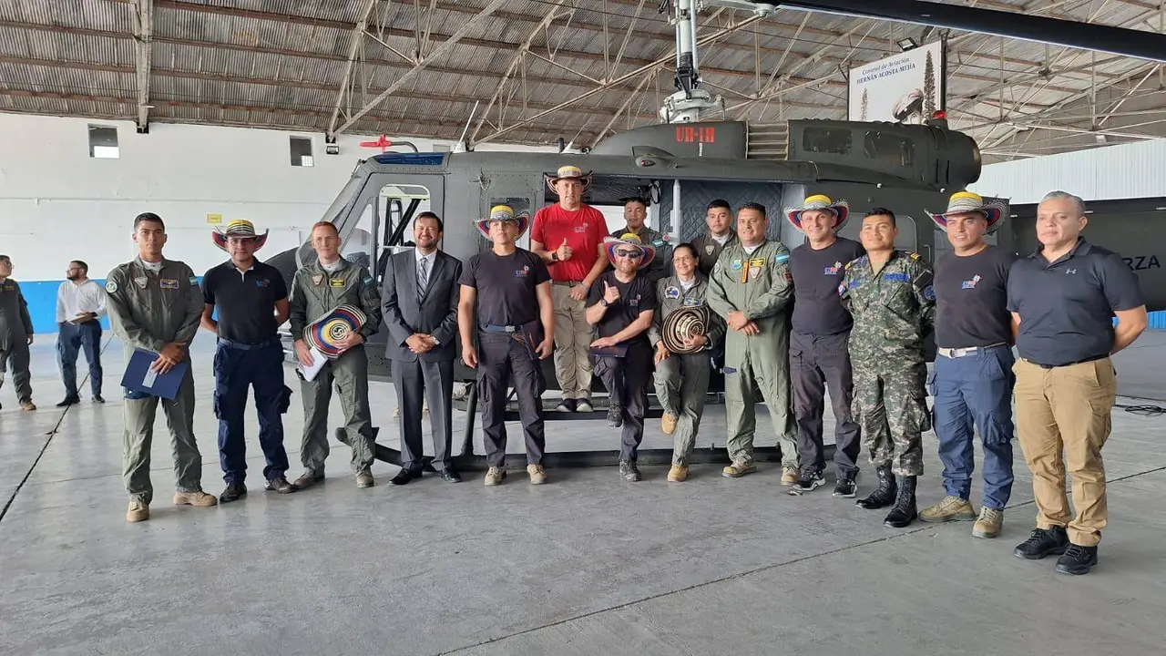 Group of uniformed personnel standing in front of a helicopter in a hangar.