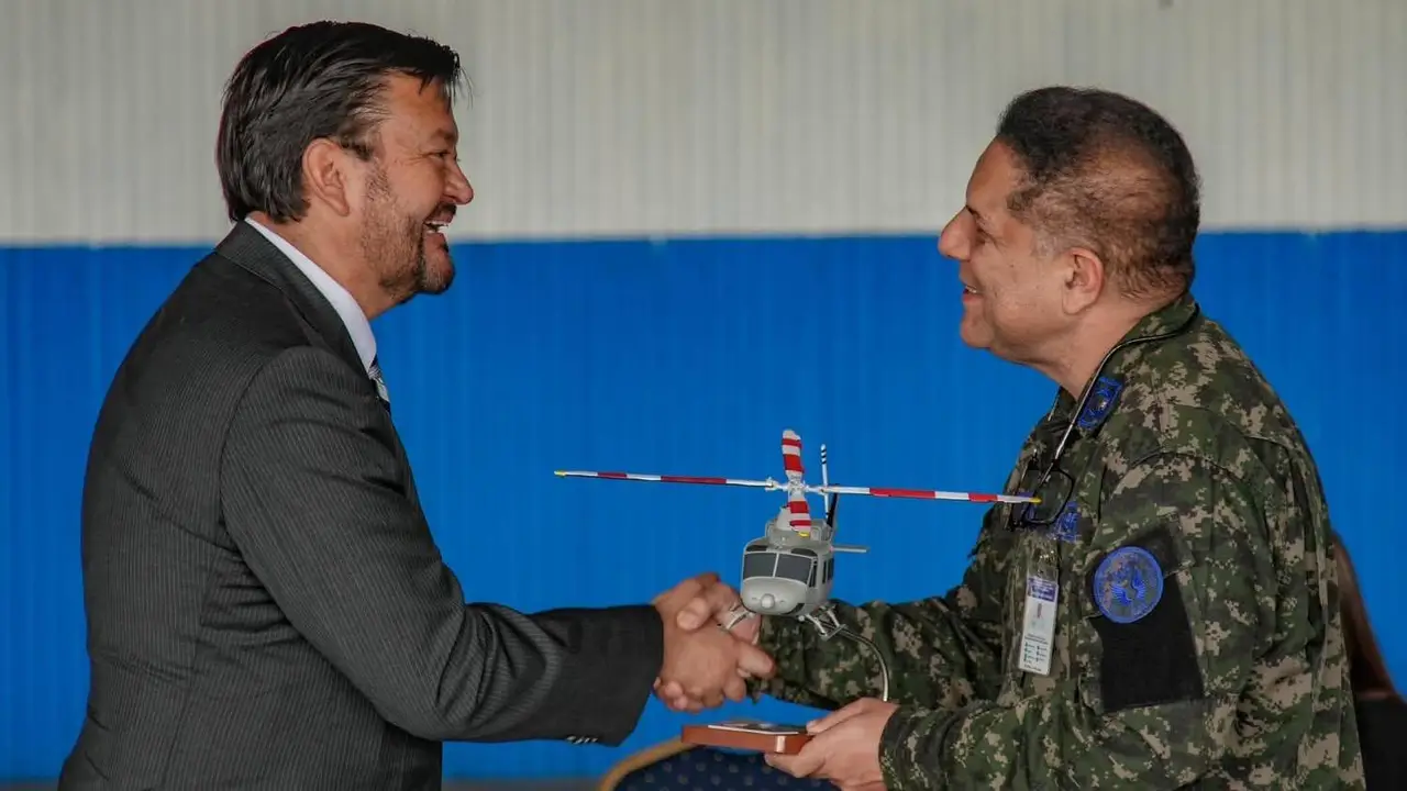 Two people shaking hands, one in military uniform, with a model helicopter above.