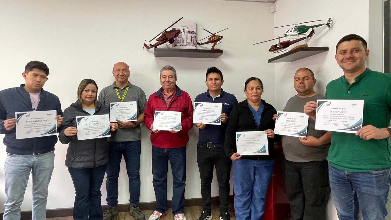 Group of individuals holding certificates, with model helicopters on the wall behind them.